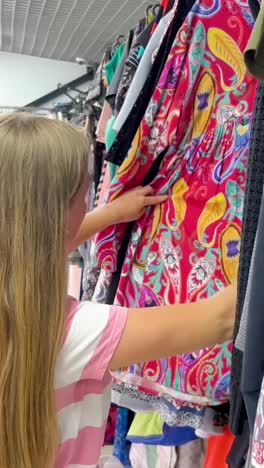 longhaired young woman buys used clothes in a clothing store black friday longhaired young woman buys used clothes in a clothing store a woman carefully examines used clothes black friday