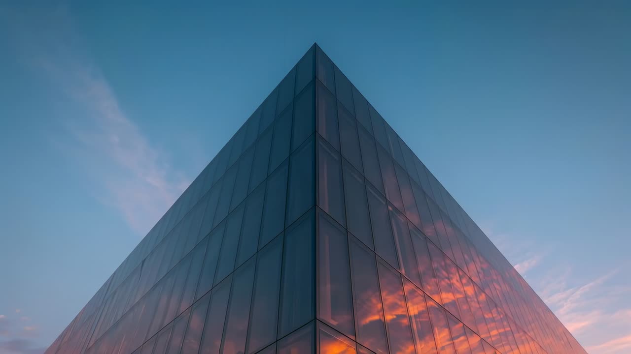 Catching lowering sun, glass corner mirroring clouds, treeline and side glass volumes at plaza