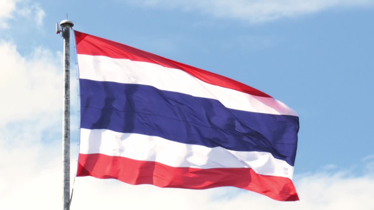 파란 하늘 과  ⁇  구름 을 배경 으로 한 기둥 에 태국 국기 를 흔들고 있다