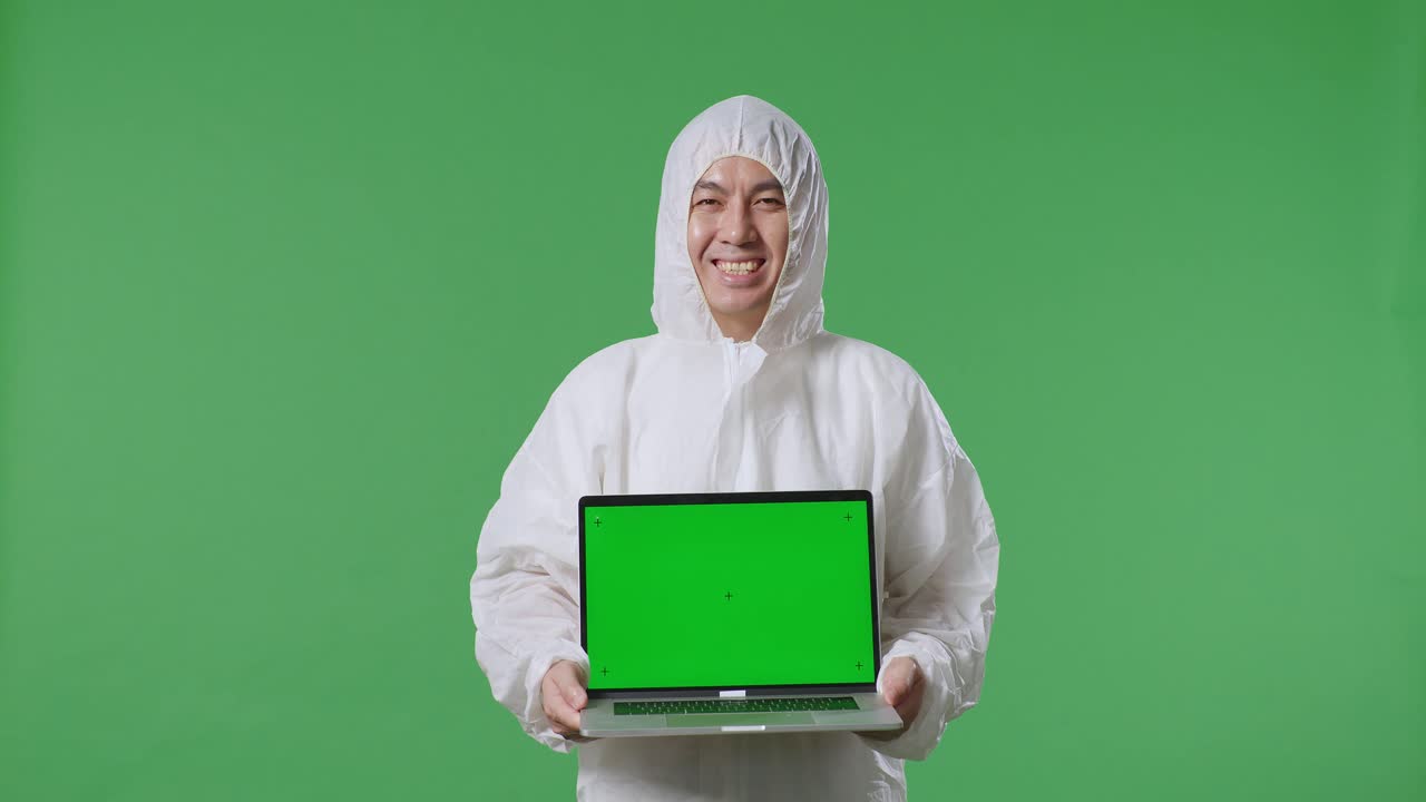 científico masculino asiático sonriendo y mostrando una computadora portátil de pantalla verde mientras está de pie en el fondo de la pantalla verde
