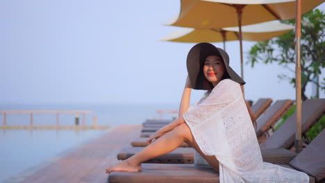 Gorgeous-woman-in-big-black-hat-illuminated-by-sunset-light,-resting-on-sunbed