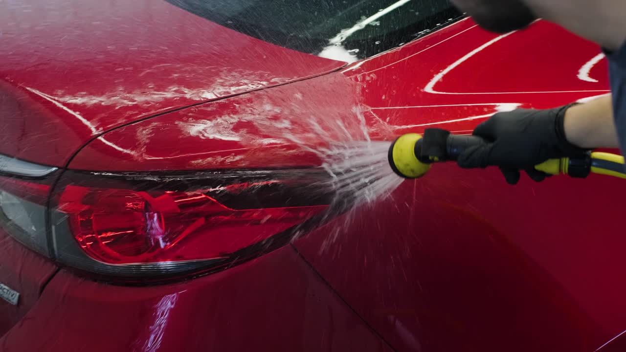 hombre trabajador lavando coche rojo en un lavado de coches.