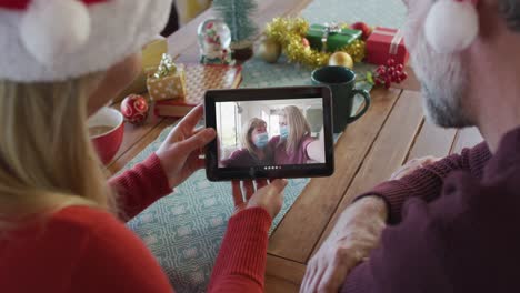 Caucasian-couple-with-santa-hats-using-tablet-for-christmas-video-call-with-family-on-screen