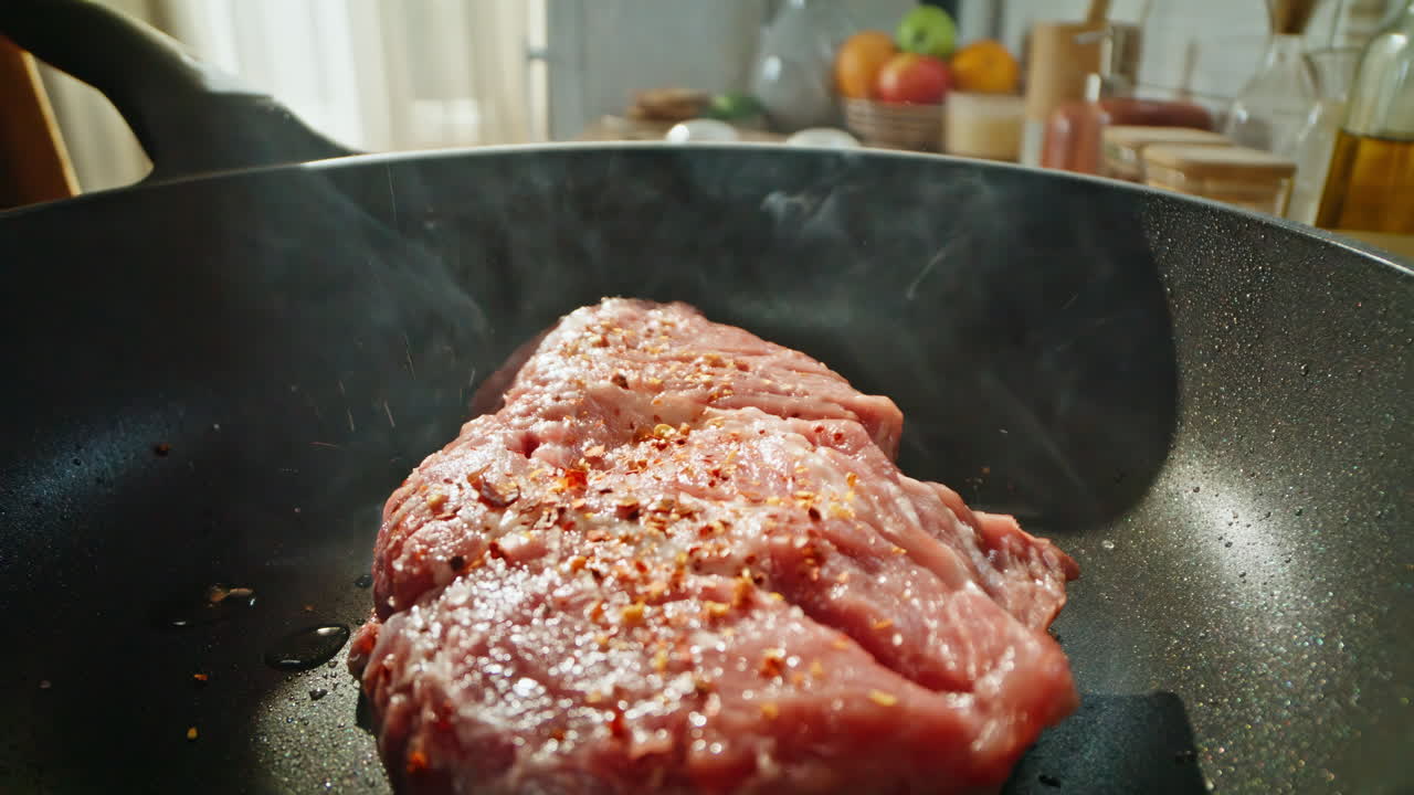 Closeup meat steak frying on hot pan surface. Unrecognizable chef seasoning beef