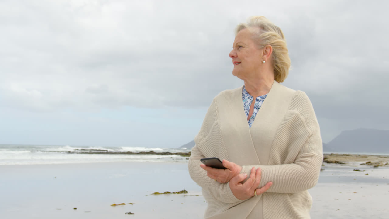 Front view of old caucasian senior woman using mobile phone at beach 4k 