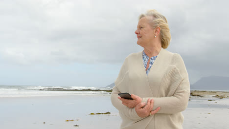 front view of old caucasian senior woman using mobile phone at beach 4k