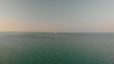 aerial tracking shot of distant ship on the arabian gulf at sunset sunrise