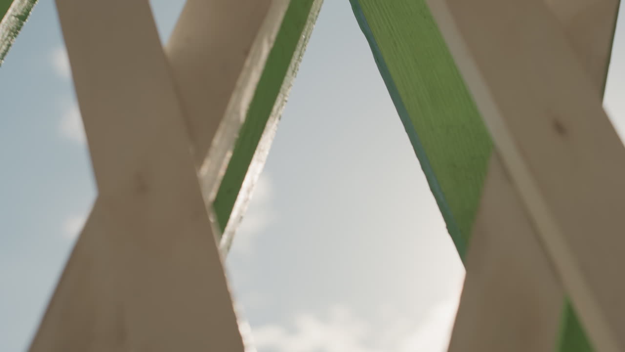 Treliça de madeira em close-up, vista do céu ensolarado com tinta verde descascando, textura áspera, reflexo solar radiante através de aberturas em forma de diamante, nuvens suaves, brisa suave implícita, ambiente doméstico, memória de casa, calmo.