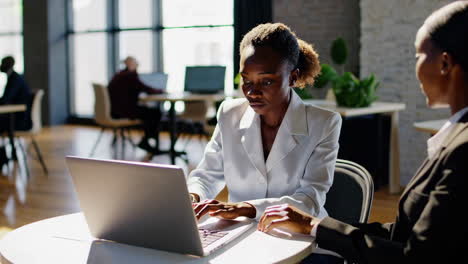 two professional women collaborating on a laptop in a modern office environment