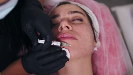 young woman is lying on the couch while professional cosmetologist in gloves is making multiple injections in woman's chin