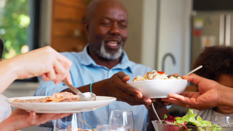 multi-generation family sitting around table serving food for meal at home