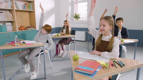 Multiethnic-Group-Of-Kids-In-Classroom-Raising-Hands-During-English-Class