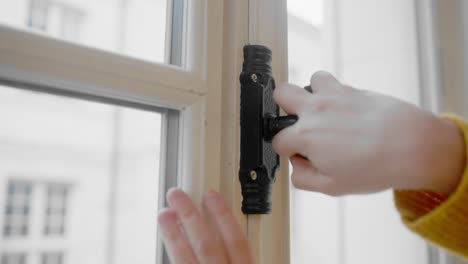 Hand-of-person-open-vintage-window-with-city-in-background,-close-up-view