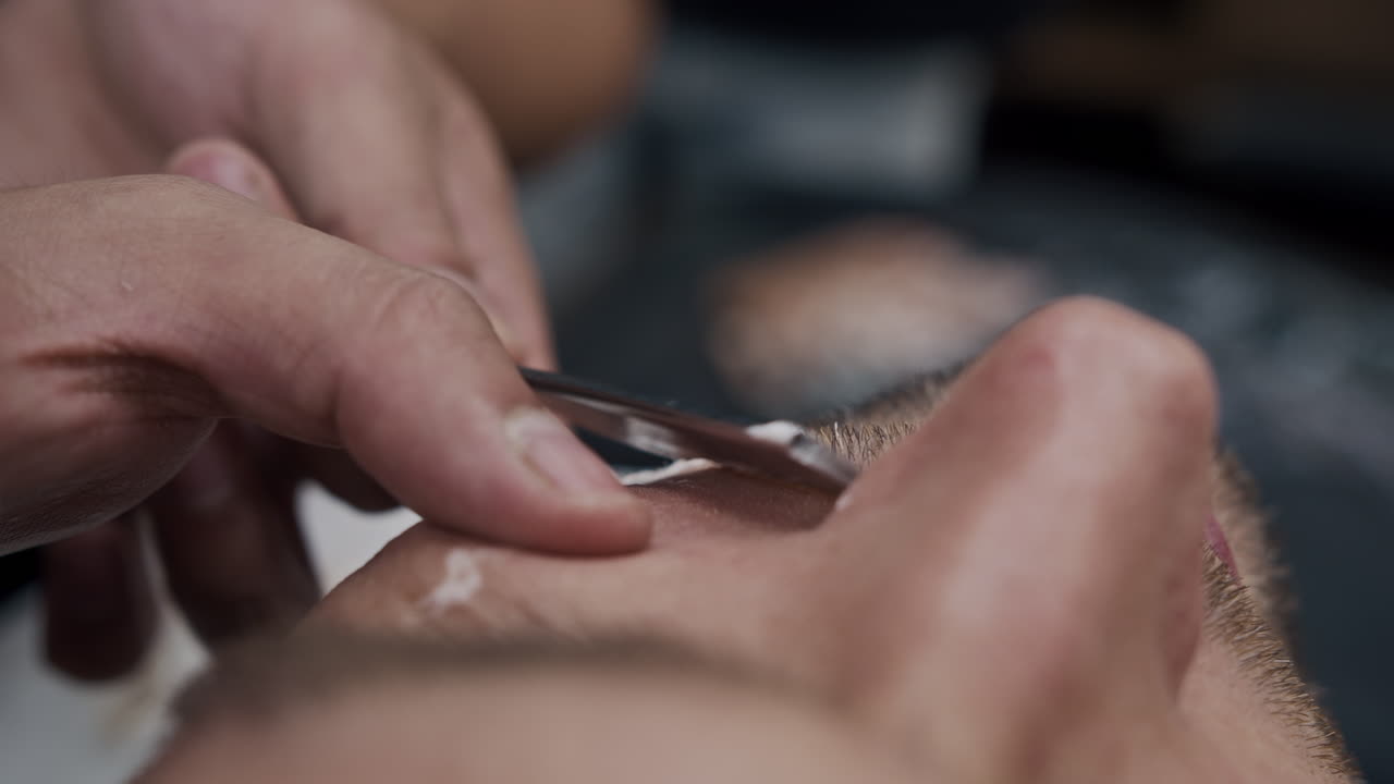 Close-up of a barber shaving a man's face with a straight razor
