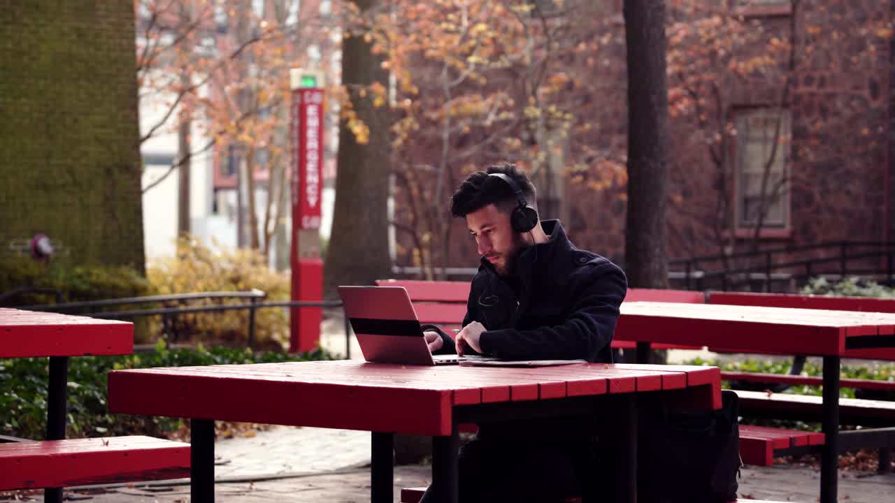 en mand, der skriver på sin notesbog, mens han lytter til musik på sine hovedtelefoner - nærbillede