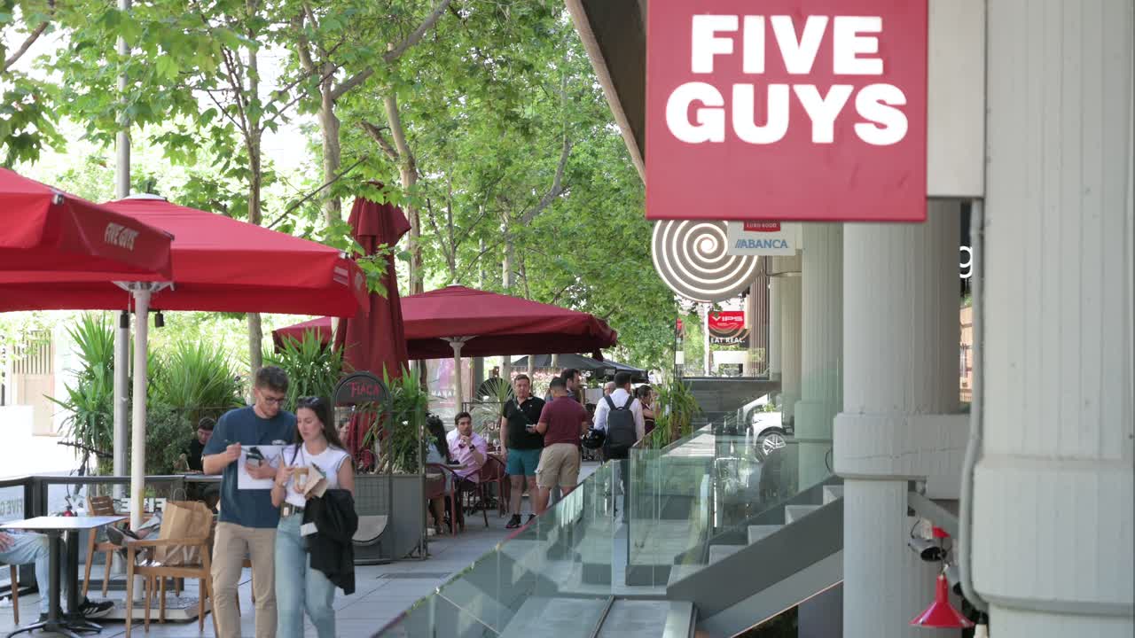 People Walking Past Five Guys Restaurant on a Busy City Street