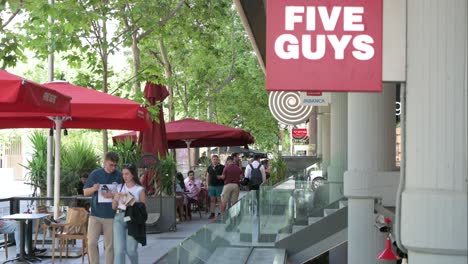 people walking past five guys restaurant on a busy city street