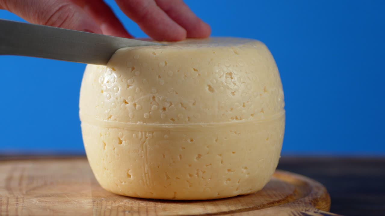 las manos de los hombres cortaron un pedazo de queso en una tabla de cortar.