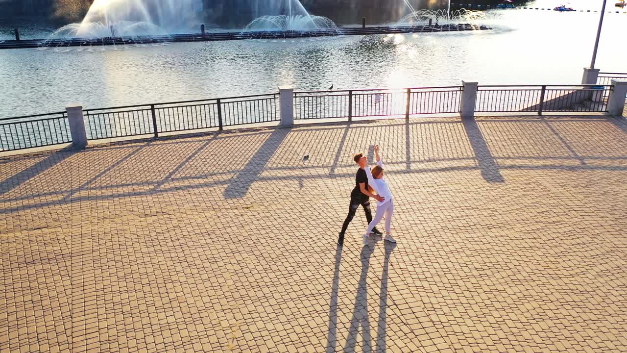 Modern dancers are dancing in the street. Urban lifestyle. Hip-hop generation. Boy's and girl's emotional moves on the video. Paving stones and young dacing couple at fontain background. Aerial view. Young beauty dances with handsome boy.