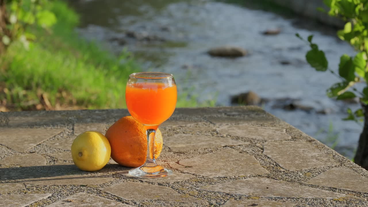 Orange juice on the stone table with flowing stream in background