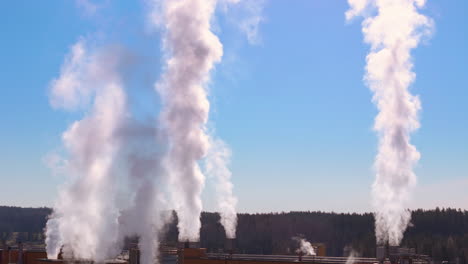 plumes of harmful factory smoke rise into clear blue sky, drone pullback view