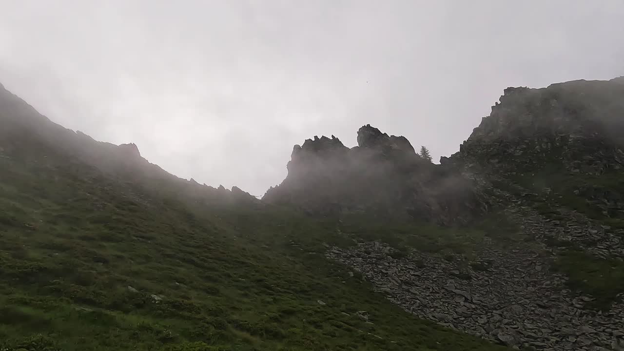 A jagged alpine ridge cuts through dense mist and low clouds in the Lepontine Alps, Piedmont, Italy, creating a dramatic and mysterious high-altitude landscape