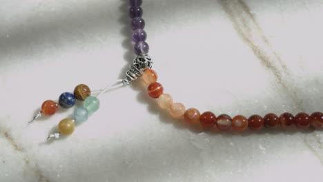 4K-Macro-dolly-shot-of-Tibetan-prayer-beads-mala-with-multiple-natural-stones-placed-on-a-white-marble-surface