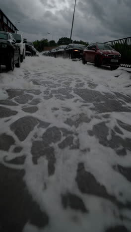 street covered in mysterious white foam with parked cars under a gloomy sky