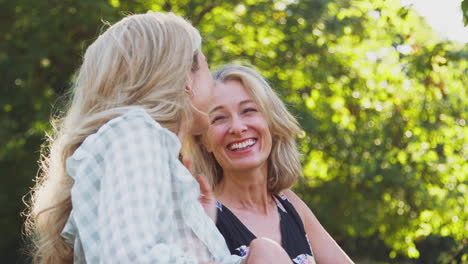 laughing mature mother with adult daughter leaning on fence walking in countryside