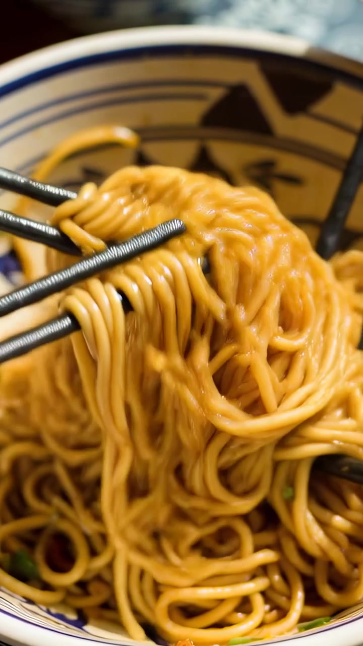 Video verticale: Bacchette che entrano da sinistra sollevando spaghetti da una ciotola decorata su un bancone per un boccone