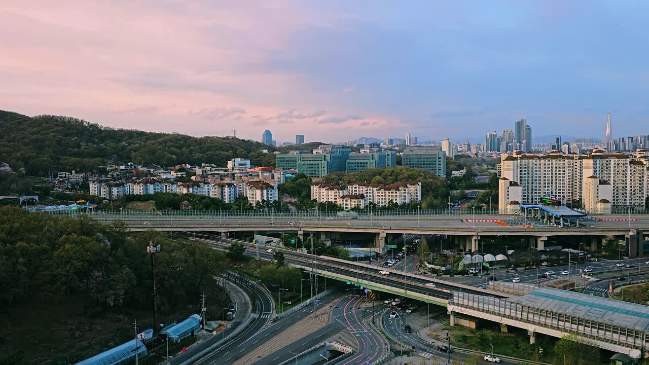 Aerial view of Seocho-gu Umyeon Tunnel entrance with urban skyline, Samsung Research and Development Center, and Lotte Tower in the distance at sunset, Seoul, South Korea