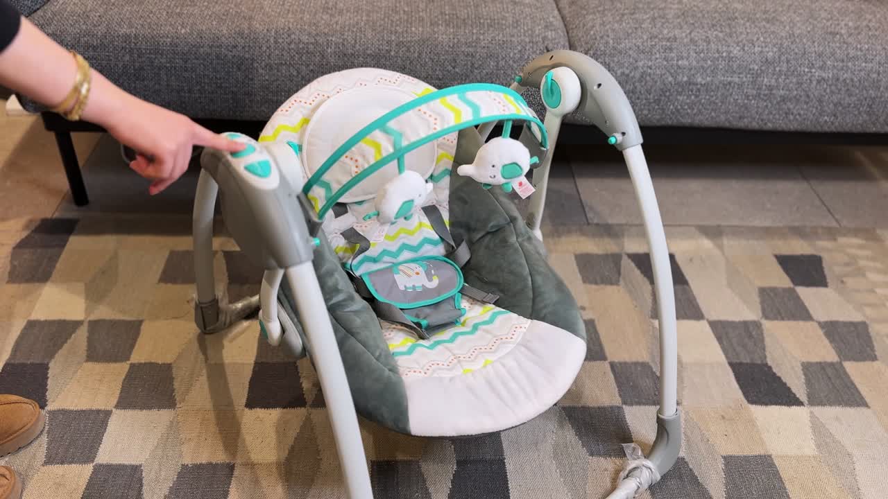 Parent pressing control button to start automatic baby swing bouncer in cozy living room. Modern nursery setup, baby care gear, and parenting lifestyle scene