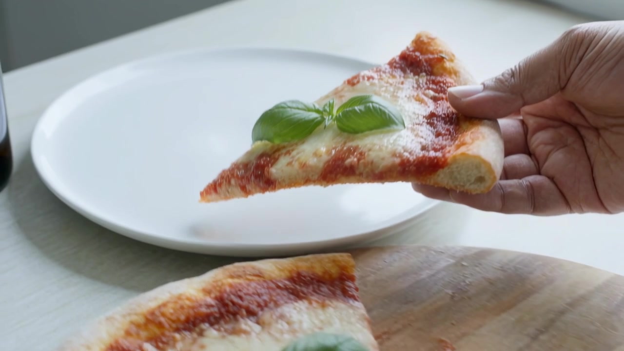 Mano destra adulta che solleva una fetta di pizza Margherita su un piatto bianco in cucina, servendo la pizza.