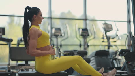 hispanic woman does exercises on the rowing machine. a girl sits behind a simulator is called a rowing machine. sitting pulls the weight of large windows and treadmills of the gym