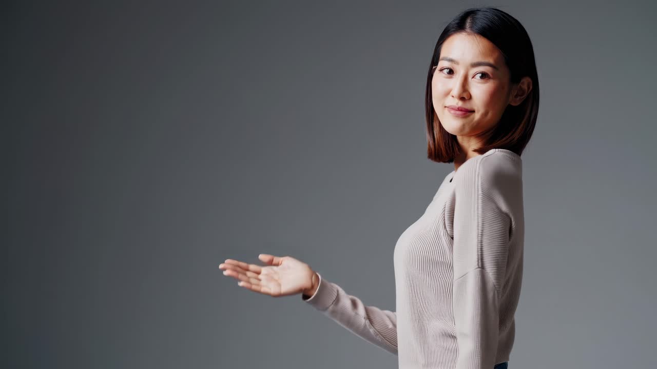 A woman smiles warmly at the camera in a medium close-up shot against a plain background