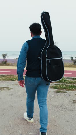 man walking with guitar on the beach