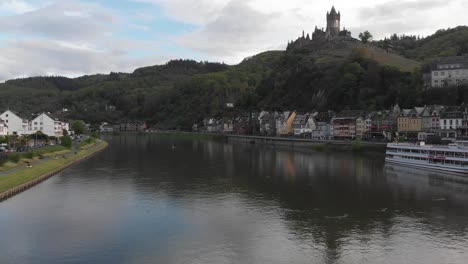 Drohne-Fliegt-Flussaufwärts-Mit-Blick-Auf-Schloss-Und-Bunte-Häuser-Am-Flussufer-In-Cochem