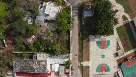 Aerial-birds-eye-overhead-top-down-panning-view-street-of-town-in-poor-tropical-region.-Tracking-cyclist-riding-around-sports-centre.-Valladolid,-Mexico