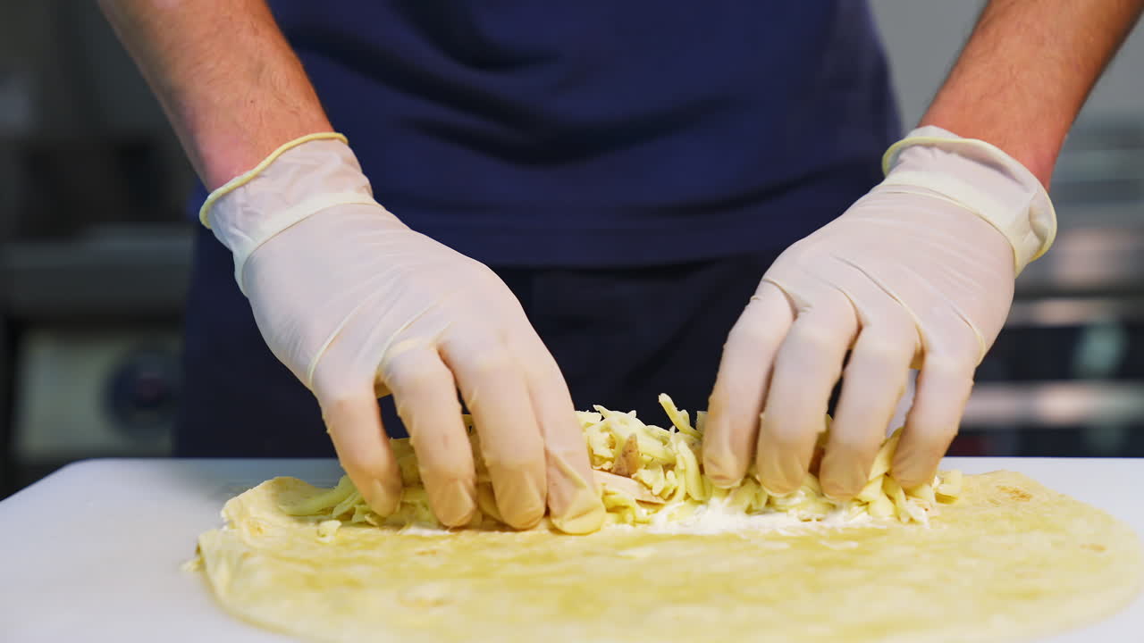 Chef prepares pita bread. Professional cook is putting cheese and chopped cucumbers into pita. Fast food. Caucasian cuisine. Close-up.