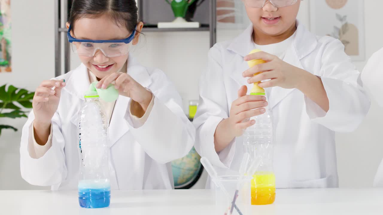 Dua mahasiswa Asia mengenakan jas lab melakukan eksperimen reaksi kimia menggelembungkan balon di botol.