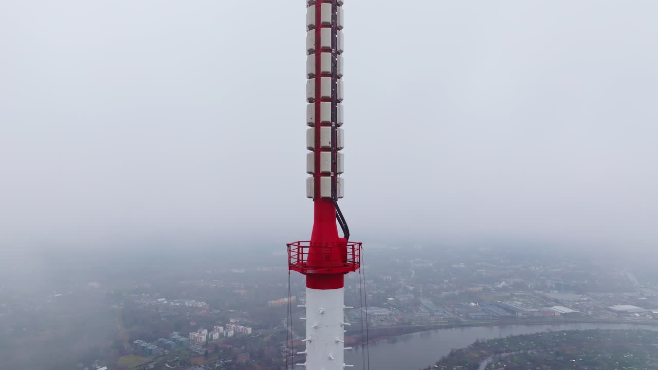 Drone descends past fog-wrapped Riga TV Tower against dull gray skyline