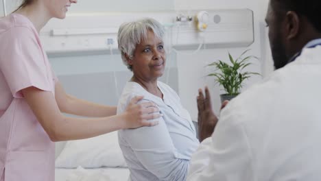 diverse male doctor and female physio treating smiling senior female patient, slow motion