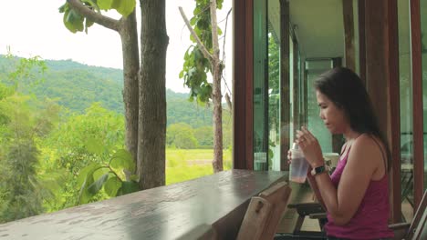 wide shot of a thai woman drinking soda at an outdoor cafe with scenic views overlooking khao yai national park