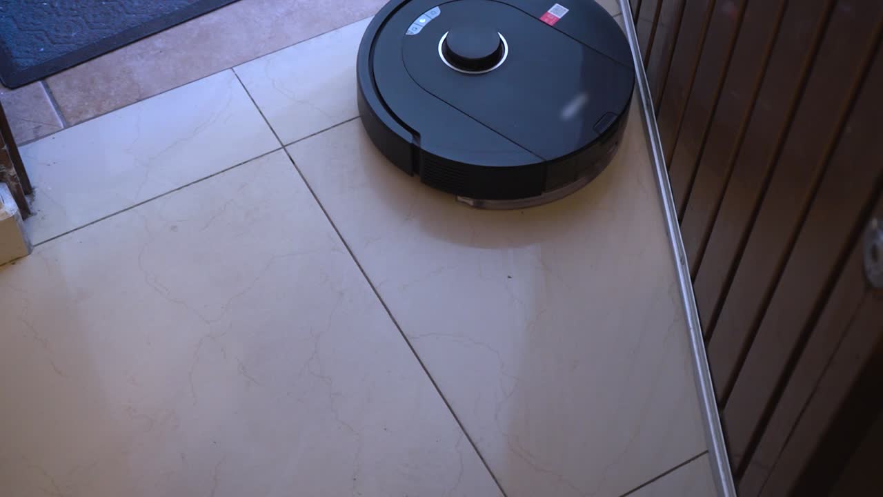 Il mocio robotizzato opera in modo efficiente nell'ingresso e nel corridoio. Scivola sul pavimento piastrellato, dimostrando le sue capacità di pulizia in un ambiente domestico.