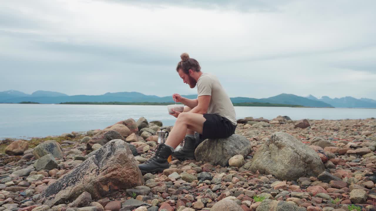 un hombre comiendo en la costa y hermosos paisajes con su perro detrás de él
