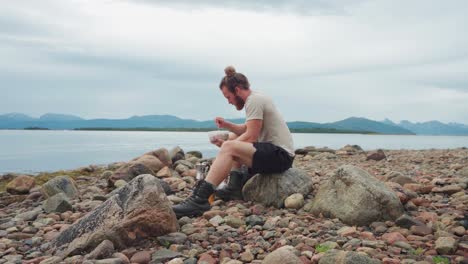 a man eating on the coast and beautiful scenery with his dog behind him