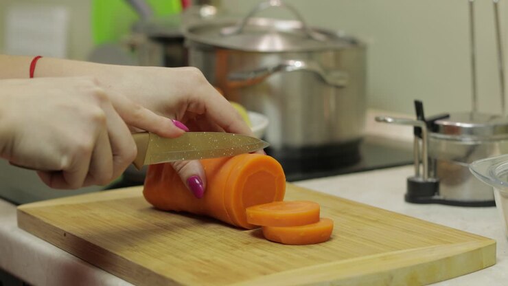 Female housewife hands slicing carrots into pieces in the kitchen