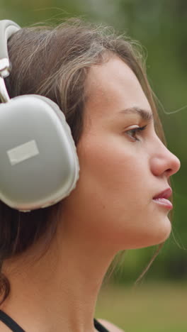 portrait of a young athlete placing headphones on her head, with a ring on her hand, standing against a blurred background of nature, she looks focused and ready for her workout or music session