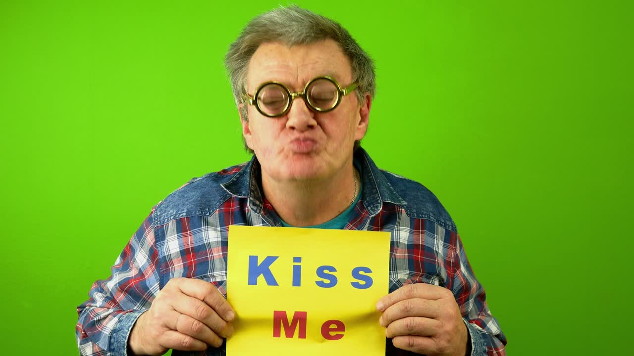 백인 성숙한 성인 남자가 어리석은 안경을 입고 미소 짓고 손가락으로 표지판 글자를 가리키며 나를 키스합니다.