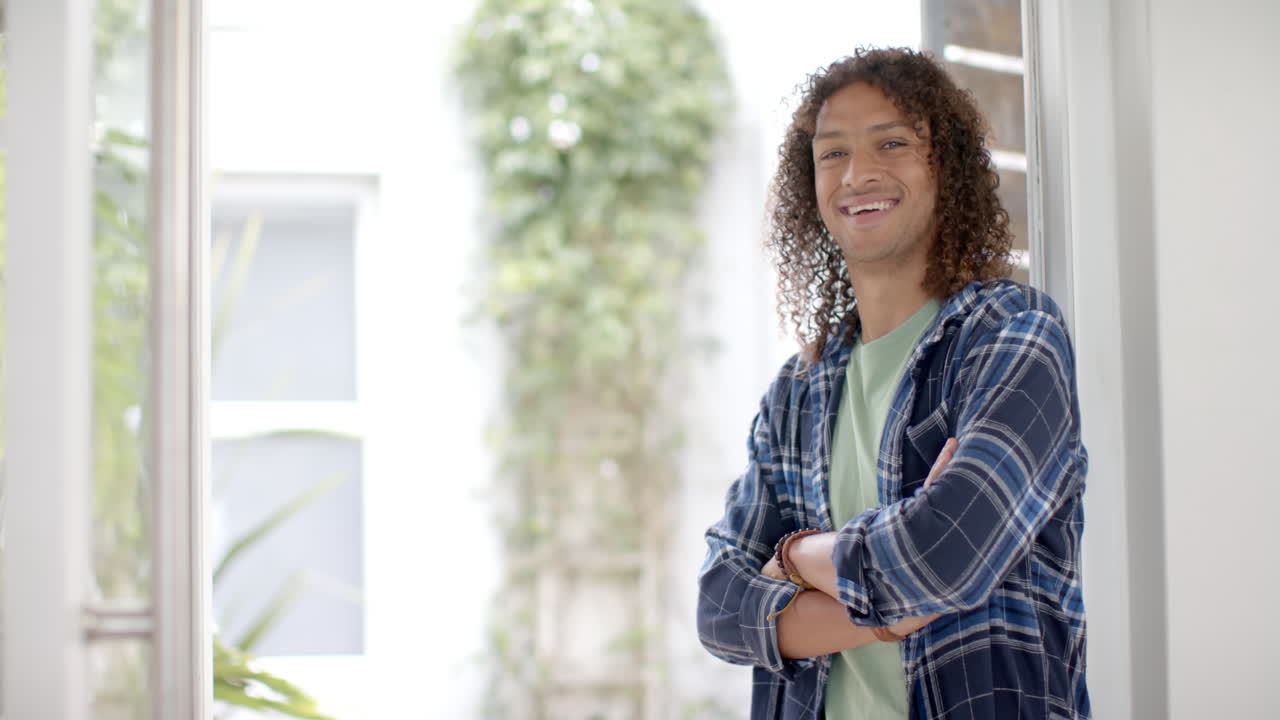 retrato de un hombre biracial con el cabello largo y rizado sonriendo en la puerta de casa, espacio de copia, cámara lenta